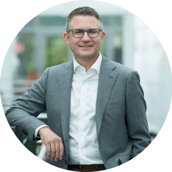 Tim Himes, a white male with grey hair, in a grey suit with no tie standing with one arm on a metal rail